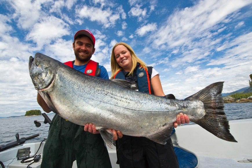 1-new Guests of Rivers Inlet Sportsman's Club fishing lodge are standing in their boat proudly holding their fresh caught massive King salmon